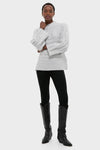 Woman in a classic Gray Cableknit Gladwyn Sweater with a mock neck and wide sleeves, paired with black leggings and knee-high boots for an effortless, high-end look.
