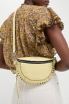 Butter Skano Fannypack in pale yellow leather, featuring a classic half-moon shape, metal studs, and an adjustable strap, exudes effortless, high-end style and fun.