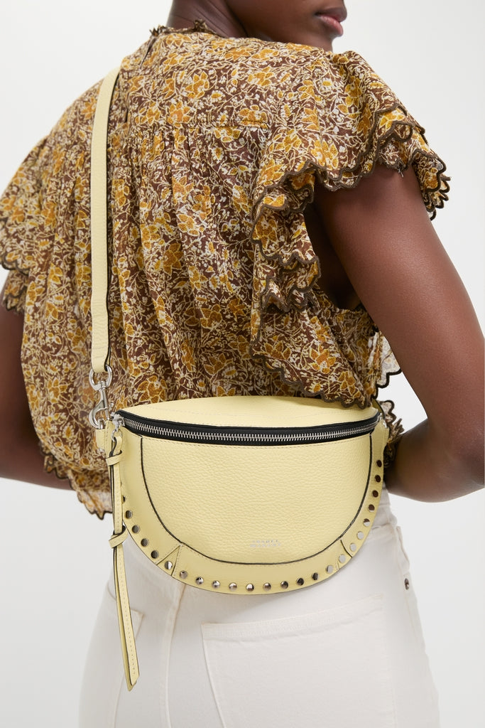 Butter Skano Fannypack in pale yellow leather, featuring a classic half-moon shape, metal studs, and an adjustable strap, exudes effortless, high-end style and fun.