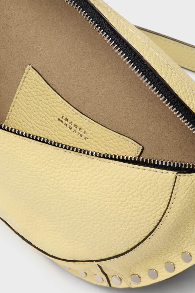 Butter Skano Fannypack: A classic, high-end pale yellow pebbled-leather bag with silver zipper, suede lining, and metal stud trim, exuding effortless style and fun sophistication.