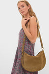 Model holding the classic Taupe Oskan Soft Zip Shoulder Strap, an effortless, high-end suede bag with a fun gold-studded detail, perfectly complementing a floral-print dress.