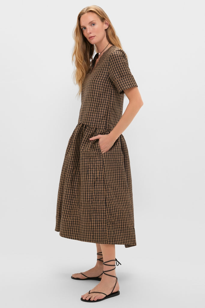Woman in profile wearing the Tobacco Brown Crinkled Taffeta Check Long Dress, featuring a classic V-neckline, drop waist, and midi length, paired with effortless black sandals.
