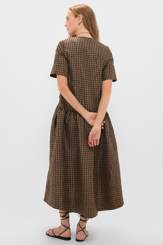 Woman in a classic, effortless Tobacco Brown Crinkled Taffeta Check Long Dress, featuring a V-neckline and drop waist, paired with black sandals.