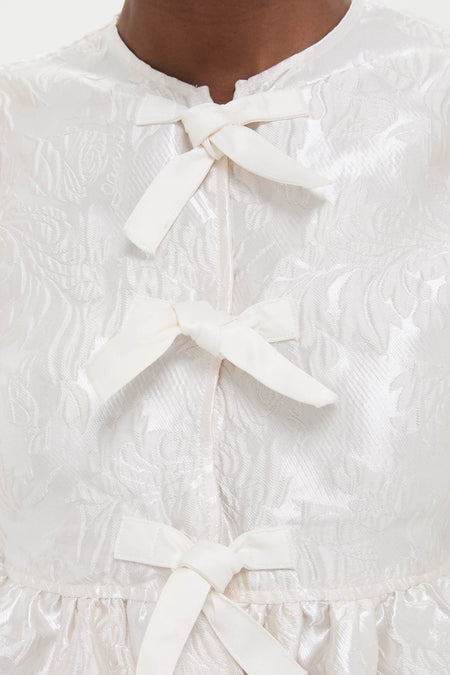 Egret Satin Cloque Peplum Blouse with classic frog closures and floral jacquard pattern, offering an effortless, high-end style for a fun, confident look.