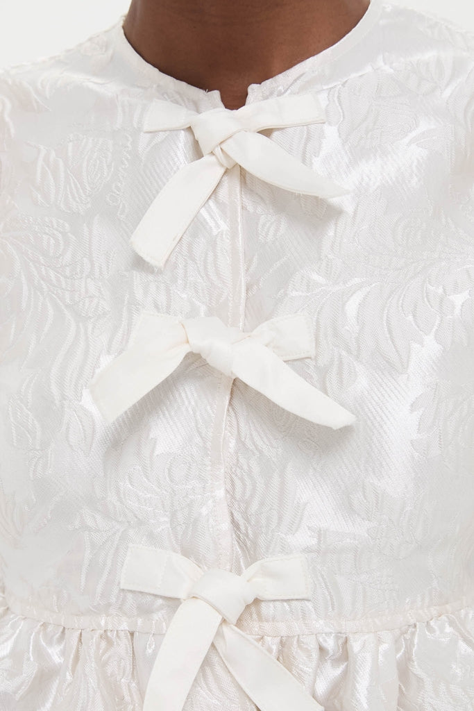 Egret Satin Cloque Peplum Blouse with classic frog closures and floral jacquard pattern, offering an effortless, high-end style for a fun, confident look.