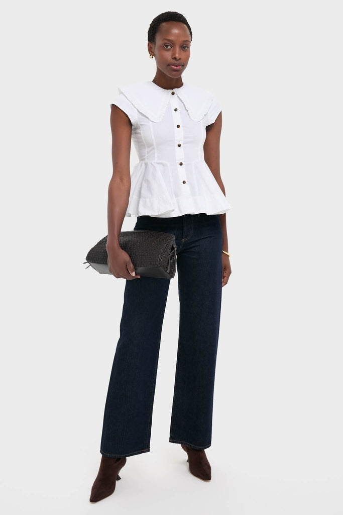 Person wearing the classic Bright White Stretch Cotton Peter Pan Collar Shirt with a peplum hem, paired with high-waisted jeans and holding a textured clutch, exuding an effortless, high-end style.