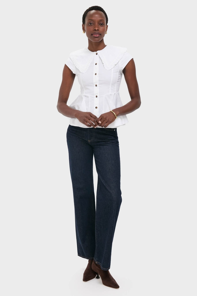 Woman models the classic Bright White Stretch Cotton Peter Pan Collar Shirt, featuring a scalloped collar and peplum waist, paired effortlessly with high-end indigo jeans and elegant heels.