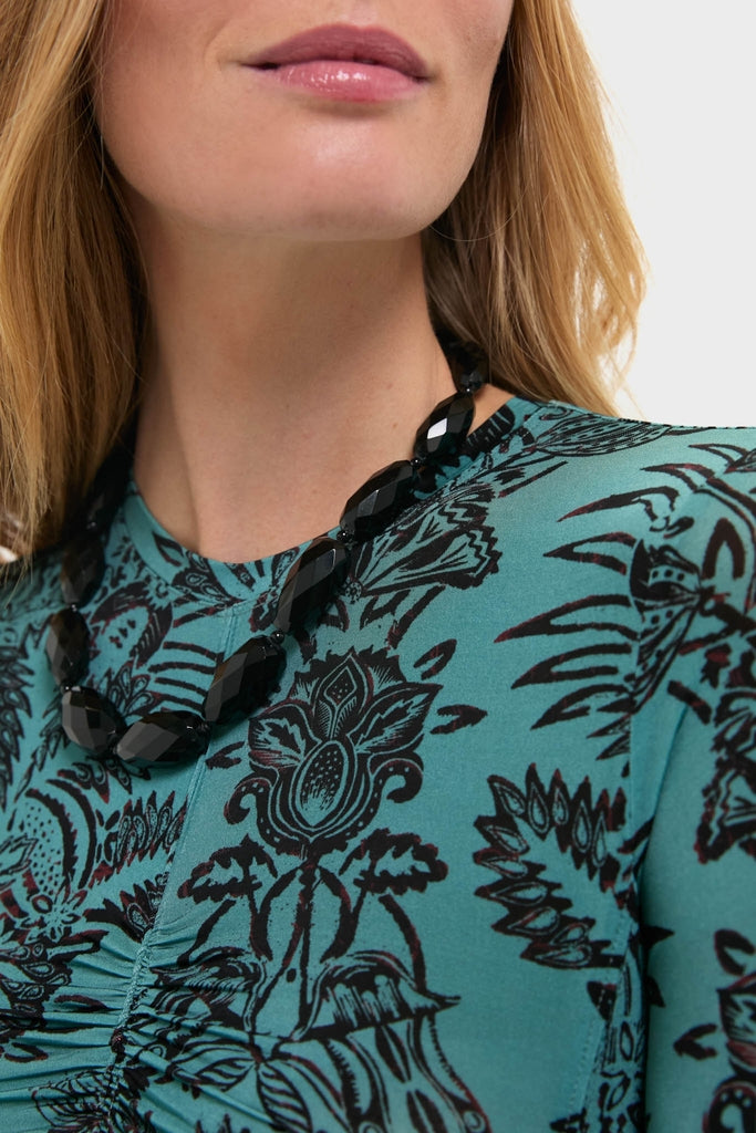 Woman wearing the Onyx Wrenlee Necklace, a chunky, faceted black bead piece, paired with a classic teal-green top, embodying effortless and high-end style.