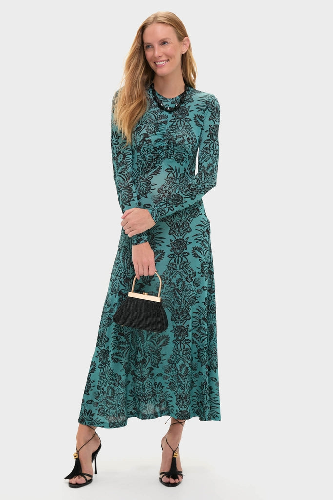 Woman in a classic teal dress with floral pattern, accessorized with an Onyx Wrenlee Necklace, exuding an effortless, high-end style. She's holding a fun, wicker-style handbag.