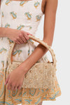 Person holding a classic, woven straw handbag with gold-tone studs, wearing a paisley dress. Showcases effortless style, complementing the high-end Pearl Necklace with Carpe Diem Charm.