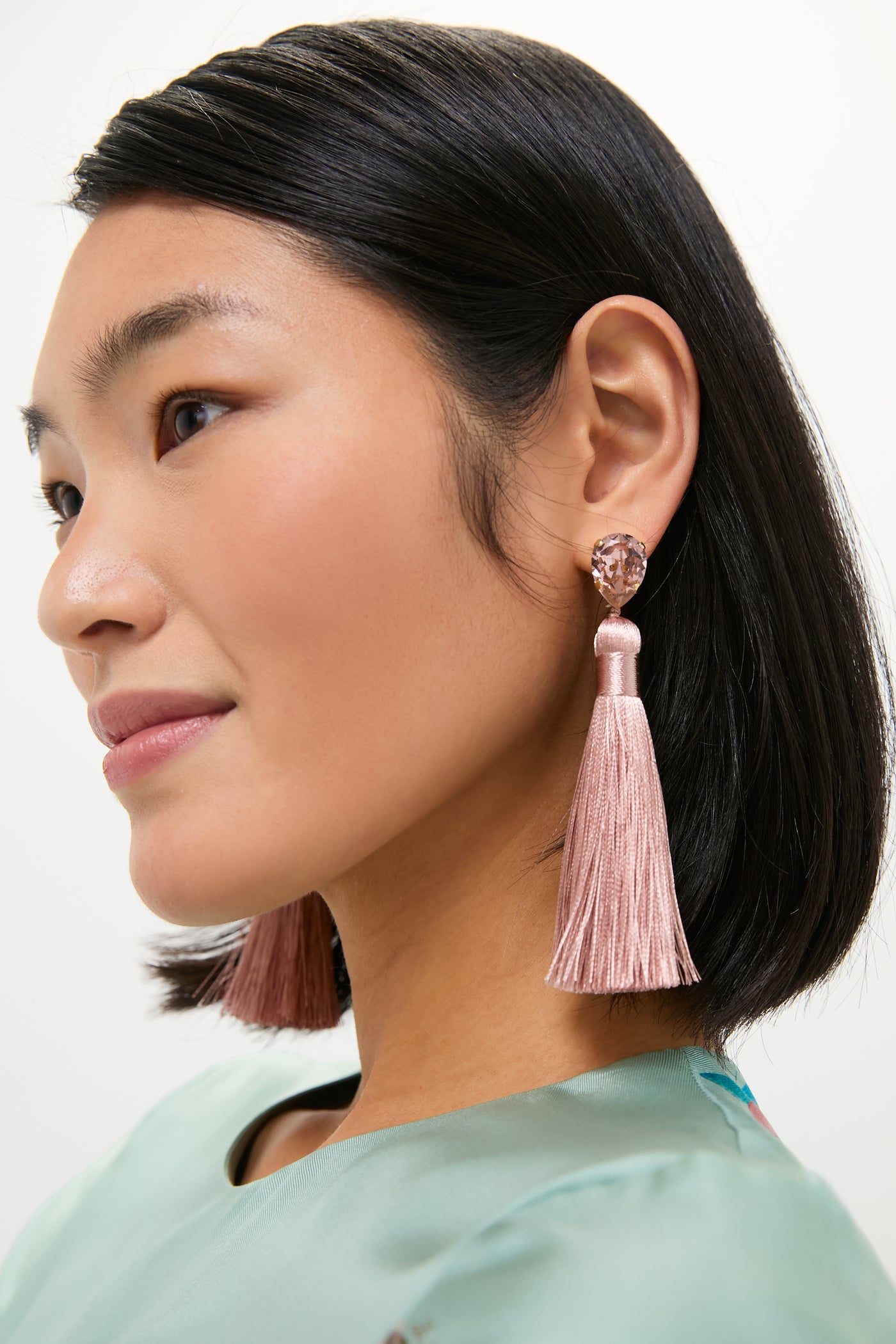 Young woman wearing the Vintage Rose Francine Earrings: teardrop crystal studs with blush-pink silk tassels, embodying classic, effortless glam for a fun, high-end look.