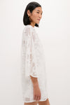 Woman in profile wearing the White Floral Lace Sidney Coverup, a classic and effortless mid-thigh dress with elbow-length sleeves, showcasing fun floral lace for a high-end look.