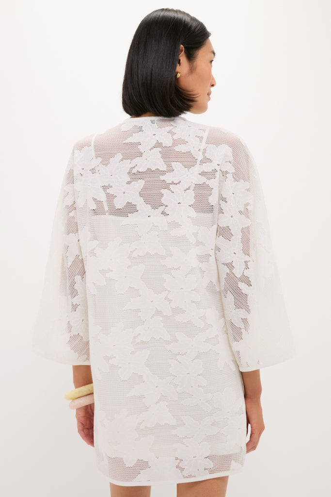 Back view of a person wearing the White Floral Lace Sidney Coverup, a classic, knee-length tunic with three-quarter sleeves and sheer floral pattern, paired with chunky bracelets.