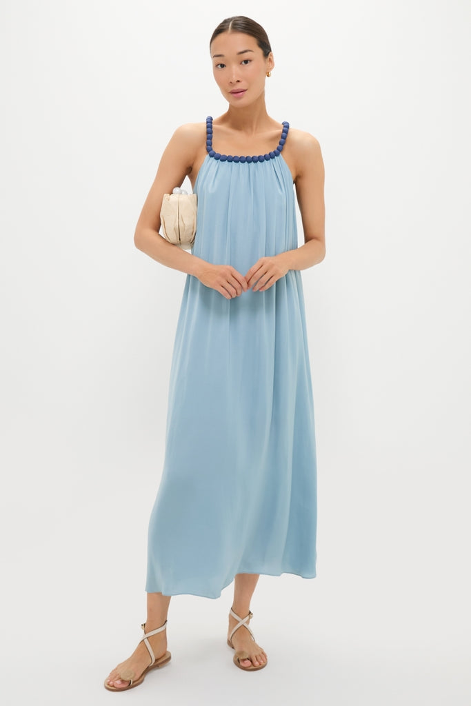 Model wearing the Light Blue Chiffon Amelia Bauble Dress, a classic and effortless maxi with beaded straps, paired with a beige handbag and neutral strappy sandals.
