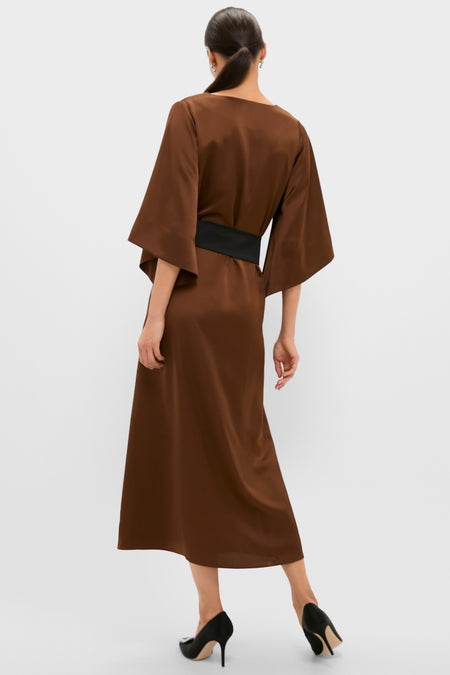 Woman in a classic, effortless Chocolate Brown Satin Emiliana Maxi Dress with kimono sleeves, a tassel-tied belt, and high-end style heels, embodying fun sophistication.