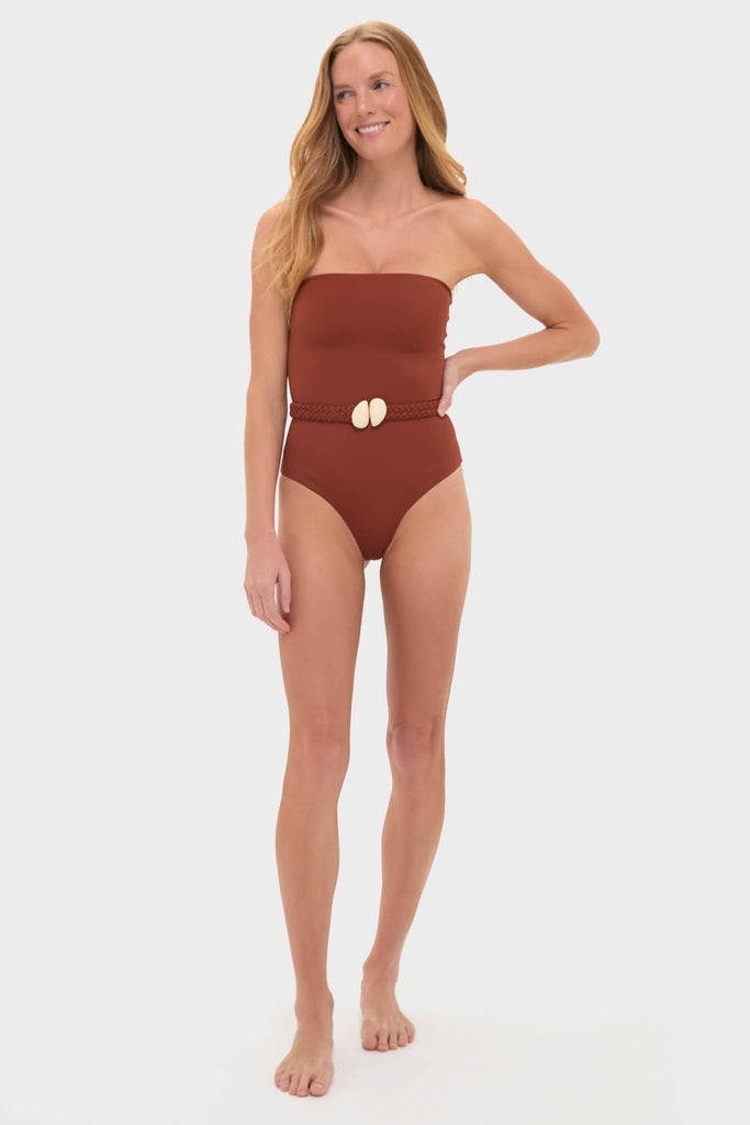 Model in a classic, rust-brown one-piece swimsuit with a braided belt and shell buckles, embodying an effortless and fun high-end style.