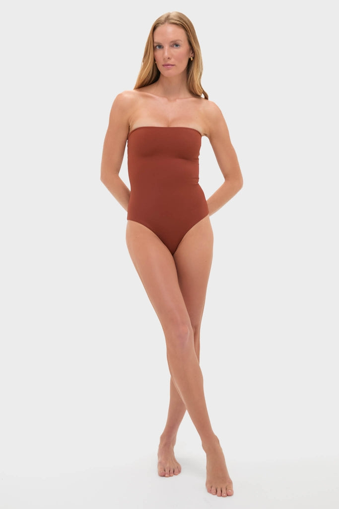 Model wears the Marsala The Classic One Piece, a strapless swimsuit with high-cut legs and braided belt, exuding effortless, high-end style with playful shell details.