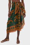Model wearing the Rust and Dark Green Dance of Pareo, a classic wrap skirt tied at the waist, paired with effortless flat sandals for a fun, high-end look.