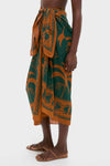 Rust and Dark Green Dance of Pareo: A classic, effortless wrap skirt with tropical print, tied at the waist, paired with fun, high-end flat sandals.