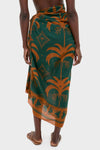 Rust and Dark Green Dance of Pareo, a classic asymmetric wrap skirt with a palm-tree motif, paired with effortless flat sandals for a high-end, fun look.