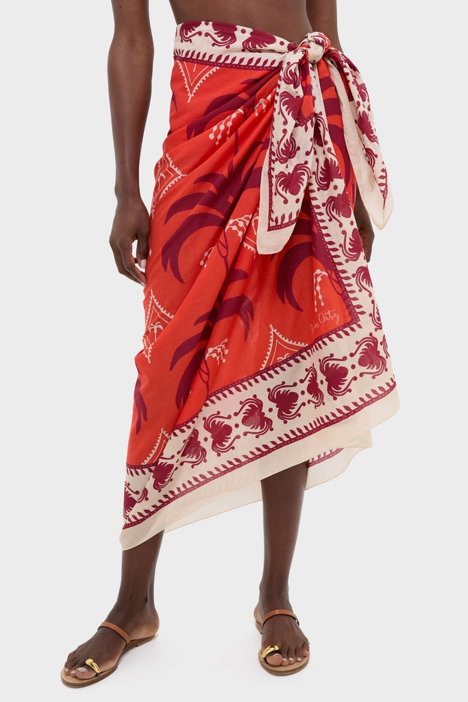 Classic and effortless Red, Ecru, and Dark Cherry Dance of Pareo in a bold print, tied at the hip, paired with simple flat sandals for a high-end, fun look.