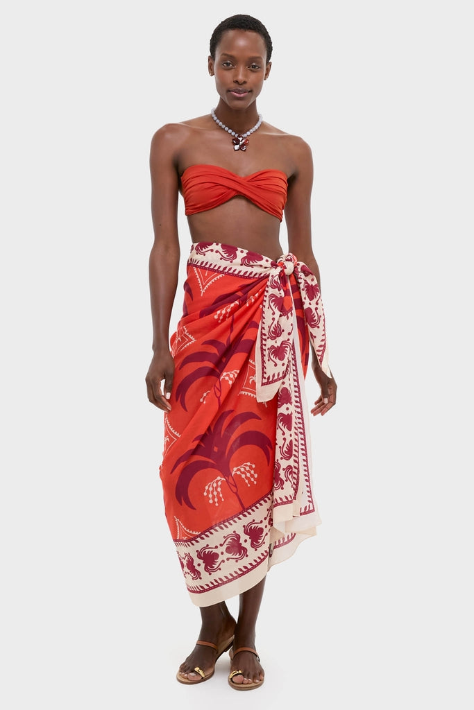 Woman in classic Dance of Pareo ensemble: twisted bandeau bikini top, matching sarong with palm print, embodies effortless style and high-end fun.