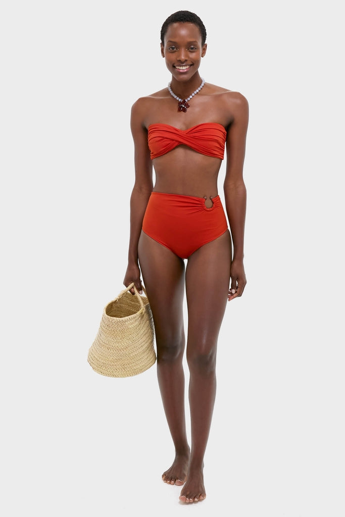 Woman in Fire Red Sea Sprite Bikini Top with twist-front design, matching high-waisted bottoms, holding a straw tote, exuding classic, effortless, and fun high-end style.