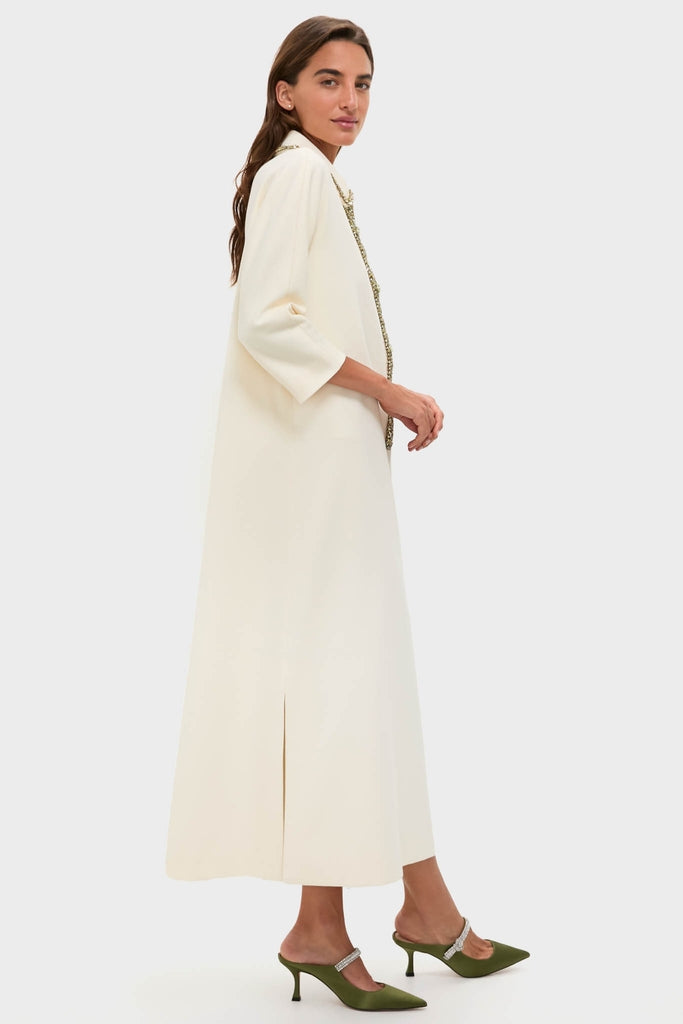 Model in profile wearing the Winter White Embellished Nicola Maxi Dress, a classic, high-end coat-dress with three-quarter sleeves, paired with effortless, fun olive green mule heels.