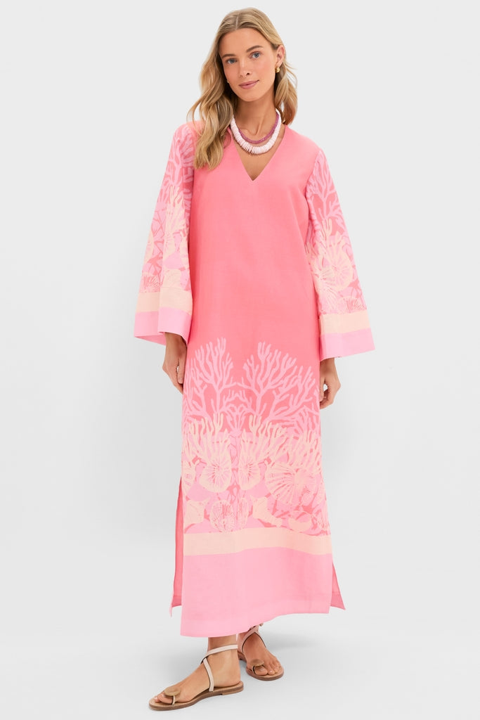 Woman models the Hopewell Coral Printed V-Neck Lorena Caftan, a classic, effortless dress with a coral-reef border, layered necklace, and sandals, embodying a fun, high-end style.