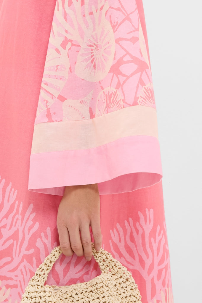 Hand holding a classic, woven straw bag, paired with the Hopewell Coral Printed V-Neck Lorena Caftan, featuring effortless, fun coral and seashell motifs on bell sleeves.