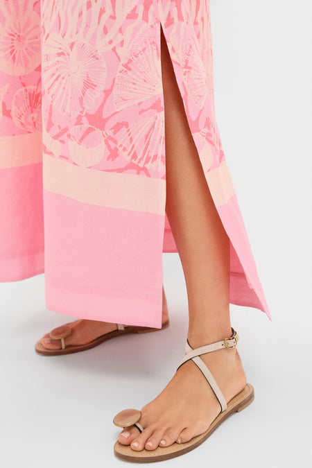 Model wearing Hopewell Coral Printed V-Neck Lorena Caftan, showcasing a classic, effortless style with a pink skirt featuring a shell-print border and side slit, paired with nude-beige toe-loop sandals.