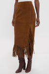 Clove Calf Roughout Suede Midi Skirt with side slit and fringe detailing, paired with knee-high leather boots, embodies a classic, effortless, and high-end style.