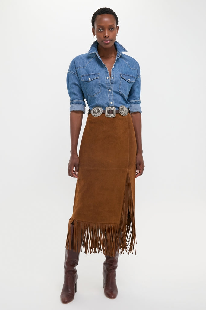 Woman in a classic Clove Calf Roughout Suede Midi Skirt with fringe trim, paired with a denim shirt and heeled boots, exuding effortless high-end style.