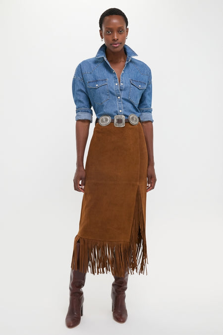 Woman in a classic Clove Calf Roughout Suede Midi Skirt with fringe trim, paired with a denim shirt and heeled boots, exuding effortless high-end style.