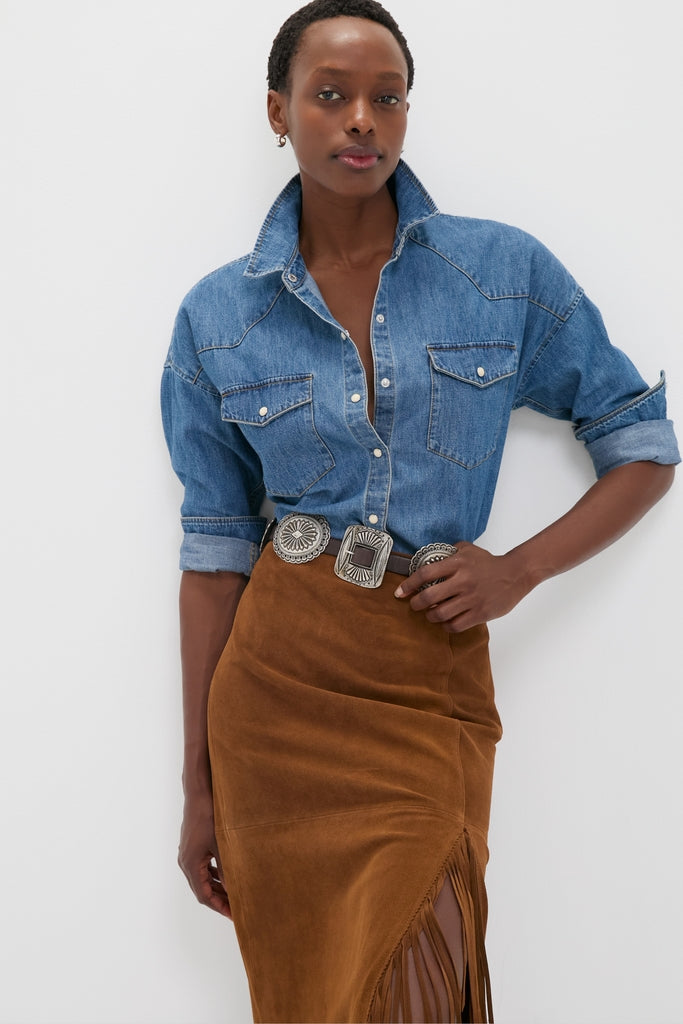 Person wearing Clove Calf Roughout Suede Midi Skirt with fringe, paired with a classic denim shirt and statement silver belt, embodying an effortless, high-end, and fun style.