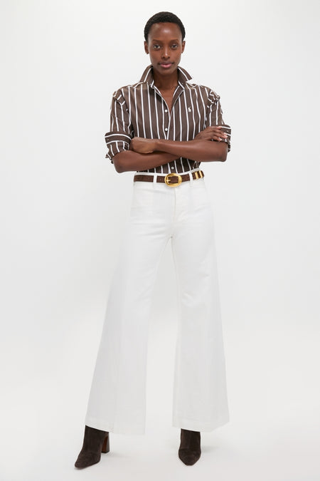 Person wearing Nevis Cotton Twill Woven Standard Flare Pants, styled effortlessly with a classic striped shirt and boots, showcasing a fun, high-end, tailored look.