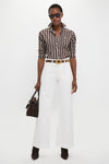 Model wearing Nevis Cotton Twill Woven Standard Flare Pants with a classic, effortless style, featuring a high-rise, wide-leg fit paired with a brown striped shirt and suede accessories.