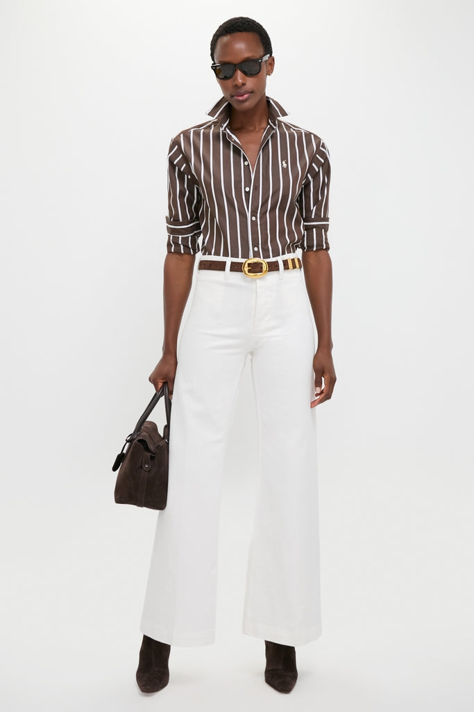 Model wearing Nevis Cotton Twill Woven Standard Flare Pants with a classic, effortless style, featuring a high-rise, wide-leg fit paired with a brown striped shirt and suede accessories.