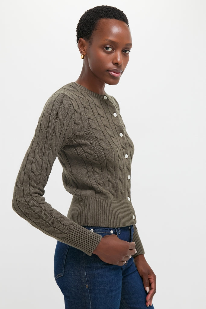 Classic Harvest Olive Cardigan with cable-knit detailing, white buttons, and embroidered pony, worn by a woman in jeans. Effortless, high-end style for everyday fun.