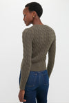 Person in profile wearing a classic, olive cable-knit Harvest Olive Cardigan with ribbed trim and signature detail, paired effortlessly with jeans for a high-end, fun look.