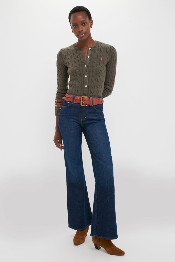 Woman models a classic olive Harvest Olive Cardigan with cable-knit details, paired with high-waisted jeans, a woven belt, and suede boots, showcasing an effortless, high-end style.