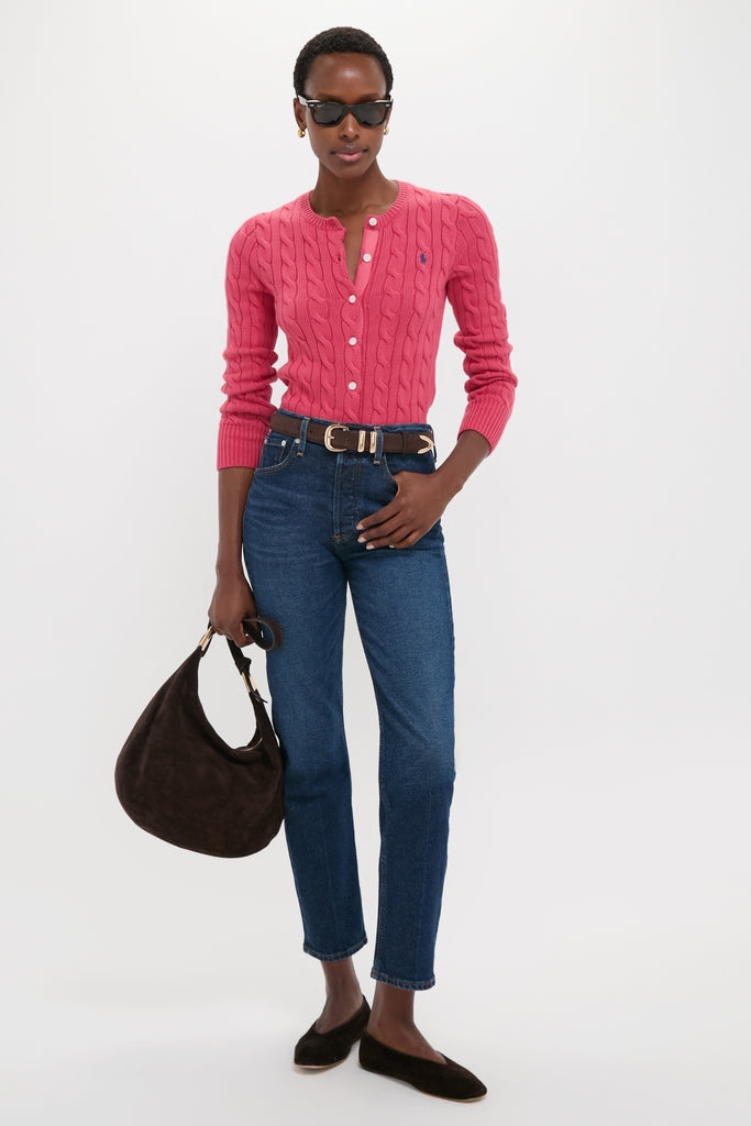 Woman wearing Nantucket Red Cardigan, showcasing its classic cable-knit design, fitted silhouette, and embroidered logo. Paired effortlessly with jeans and brown suede accessories for a fun, high-end look.