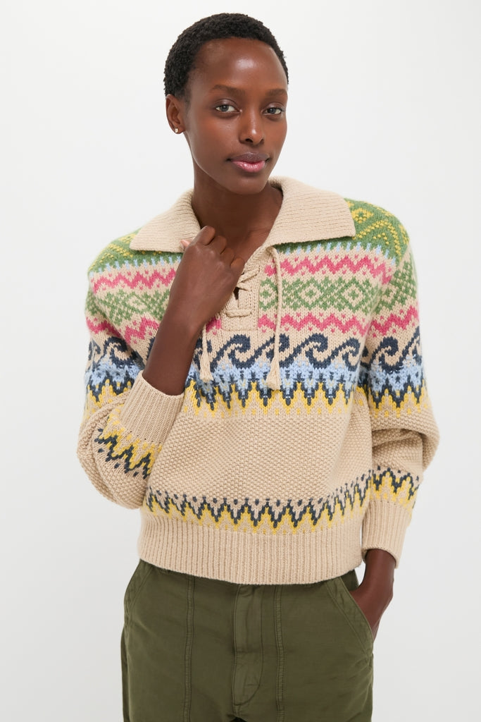 Young person in a classic, high-end Tan Multi Cotton Wool Blend Long Sleeve Tie Pullover with vibrant Fair Isle patterns, embodying effortless style and fun, paired with olive-green pants.