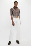 Model in a classic Dark Brown and White Stripe Long Sleeve Button Down, paired with high-waisted white trousers and suede ankle boots, exuding effortless, high-end style.
