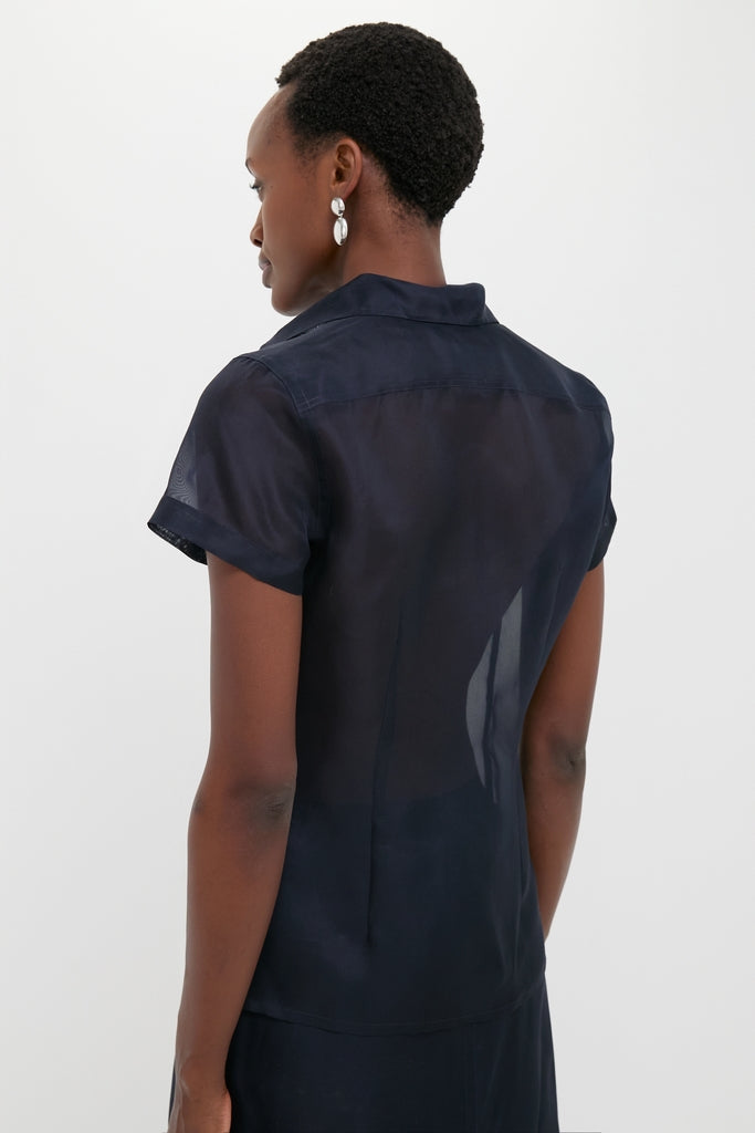 Back view of a model in an Atlantic Silk Organza Woven Short Sleeve Button Down, showcasing its classic and effortless sheer design with tailored details and silver accessories.