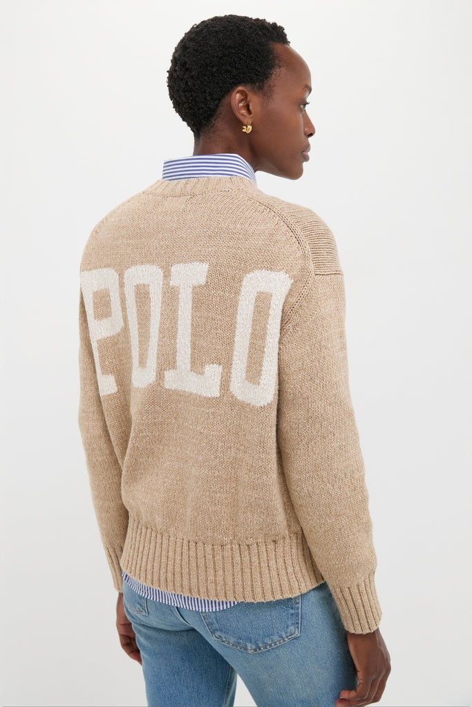 Person in a sand-beige Tan Heather Cotton Long Sleeve Crewneck sweater with POLO on back, over a striped shirt and jeans, embodying classic, effortless style.