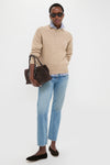 Woman wearing Tan Heather Cotton Long Sleeve Crewneck over a blue-striped shirt, styled with jeans and suede flats, embodying classic, effortless, high-end fashion.