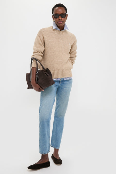 Woman wearing Tan Heather Cotton Long Sleeve Crewneck over a blue-striped shirt, styled with jeans and suede flats, embodying classic, effortless, high-end fashion.