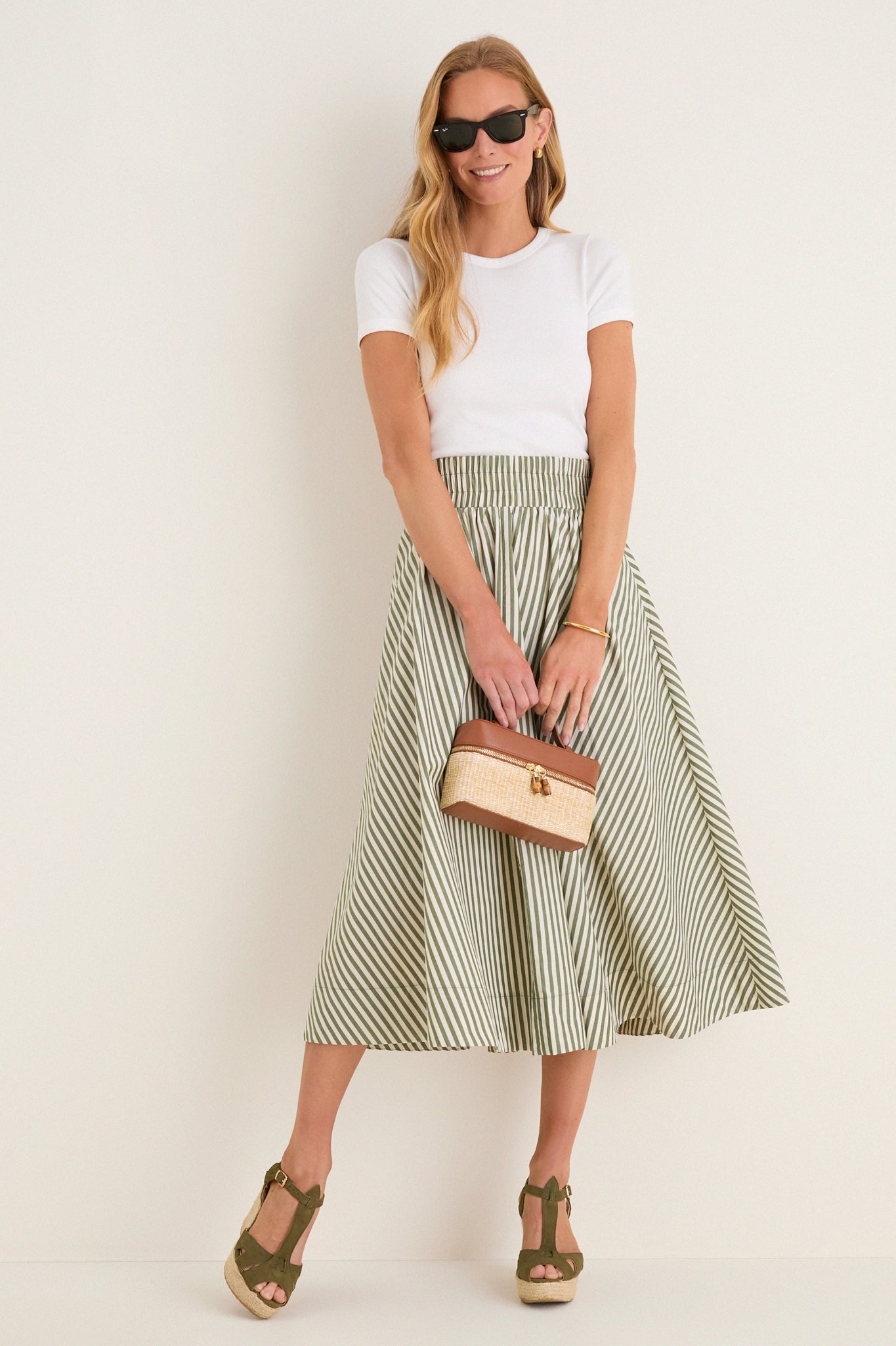 Model wearing Clover Suede Jules Espadrilles, classic olive-green wedges with jute platform, styled with a chic A-line skirt and accessories for an effortless, high-end summer look.