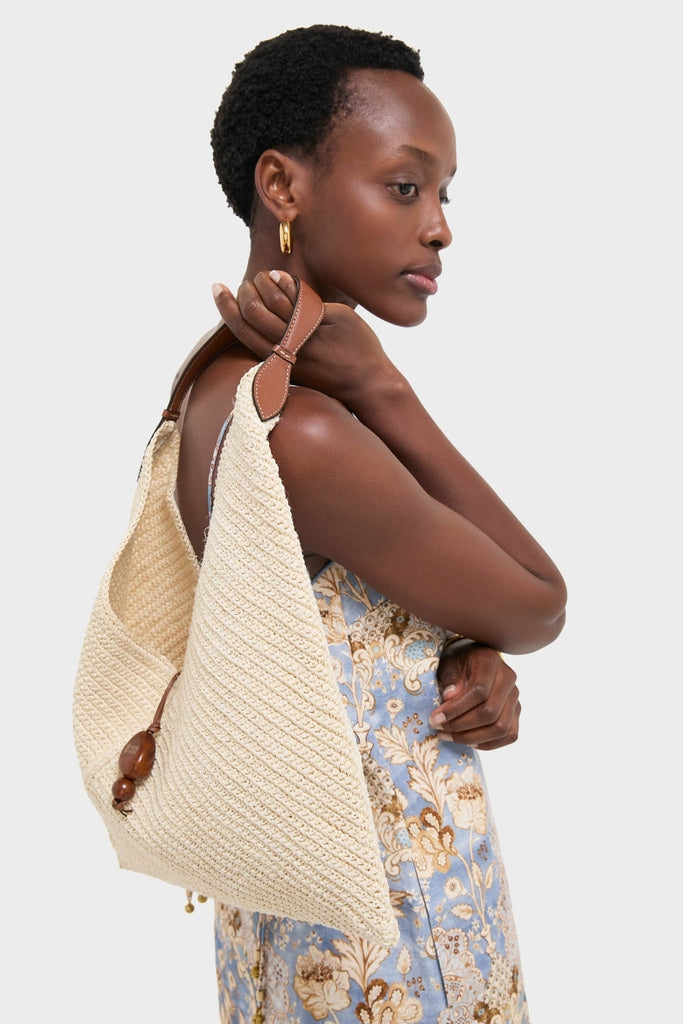 Woman holding the classic Natural Fique Large Origami Shoulder Bag, featuring a tan leather strap and wooden bead detail, paired effortlessly with a floral sundress for high-end style.